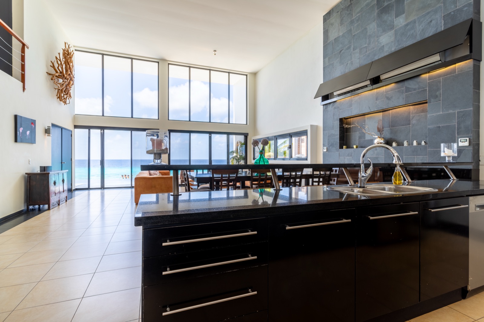 Luxury Bonaire villa great room with a gourmet kitchen island, double-height ceilings, and a wall of windows with panoramic ocean views and direct beach access.